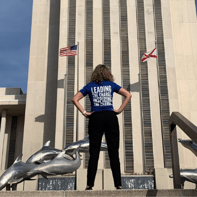 back of a person wearing a tee shirt with writing on it standing in front of a building